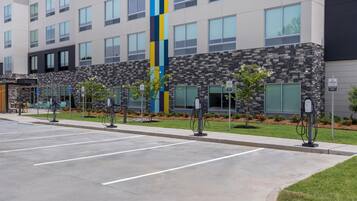 Un hotel con múltiples estaciones de carga para vehículos eléctricos, un estacionamiento y un edificio de fachada moderna.
