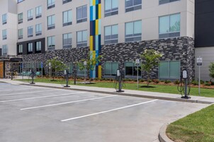 Un hotel con múltiples estaciones de carga para vehículos eléctricos, un estacionamiento y un edificio de fachada moderna.
