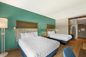 Habitación de hotel con dos camas, un escritorio, una silla y un armario.
