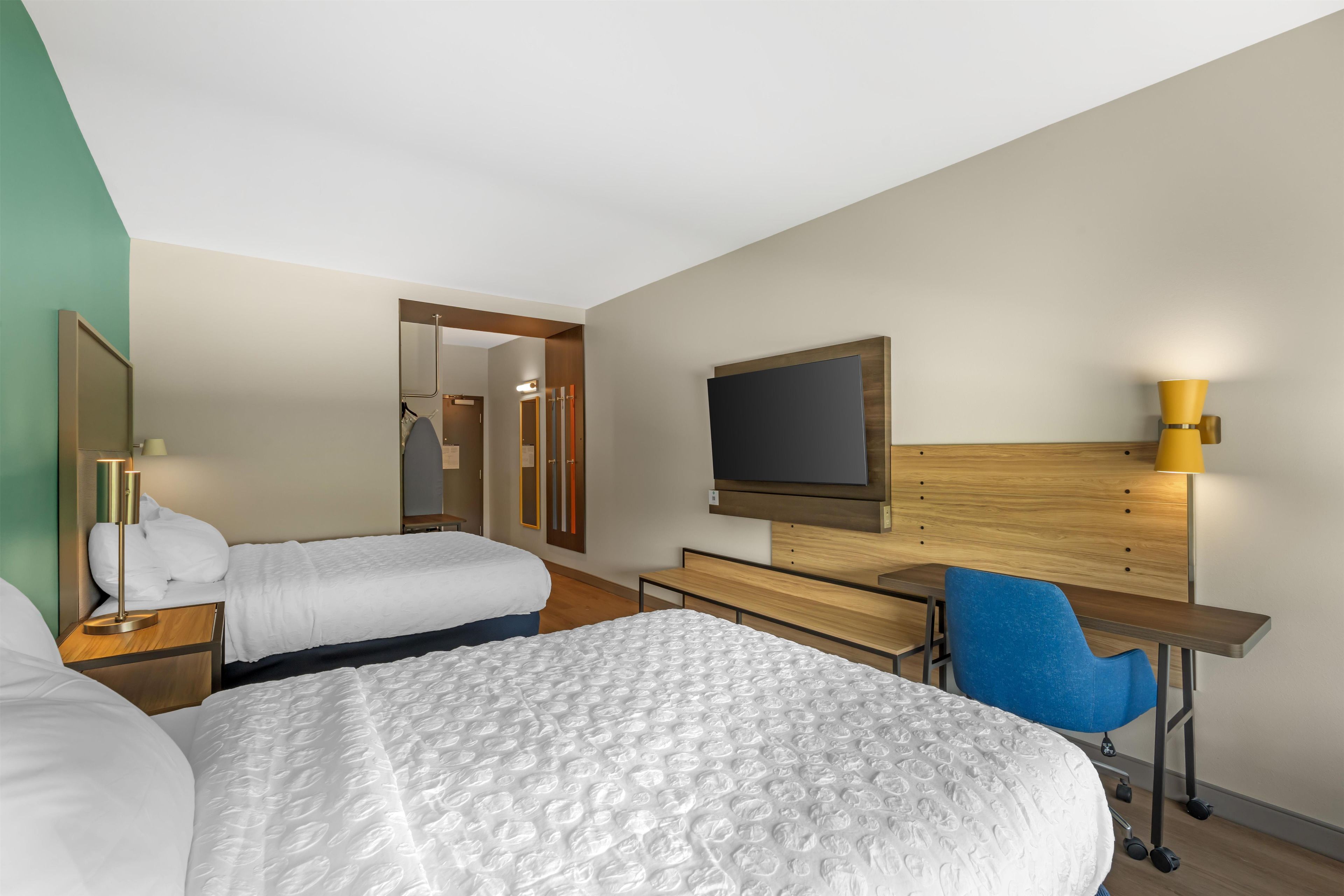 A hotel room with two beds, a desk, a chair, a TV, and a mirror.
