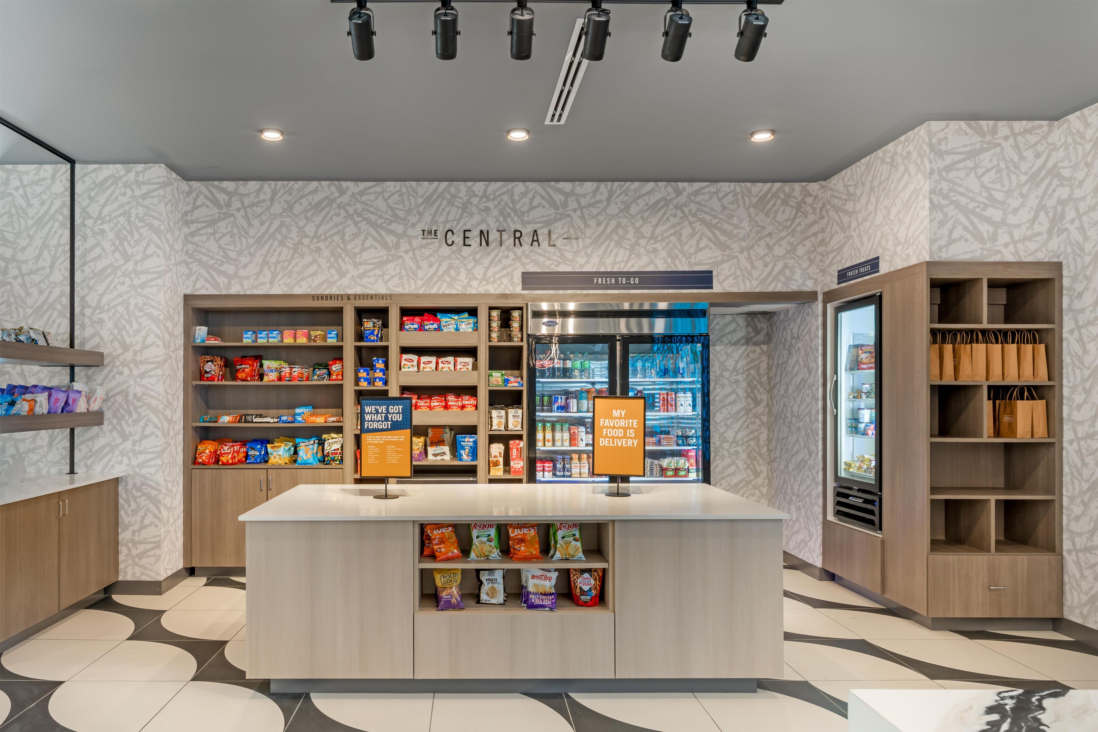 A snack bar with a variety of packaged foods, a refrigerated section, and a sign indicating a delivery service.