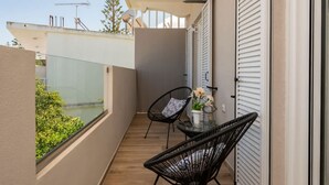 A balcony with two black wicker chairs, a small table with a vase of flowers, and a view of greenery and buildings. - Villy Suites II - Zante Lux Suite Near the Beach (Zakynthos)