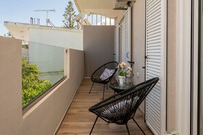 Ein Balkon mit zwei schwarzen Korbstühlen, einem kleinen Tisch mit Blumenvase und Blick auf Grünflächen und Gebäude.