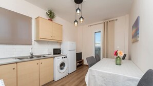 A compact kitchen with a washing machine, a microwave, and a refrigerator. There is a dining area with a table and chairs, and a small plant on the wall. - Villy Suites II - Zante Lux Suite Near the Beach (Zakynthos)