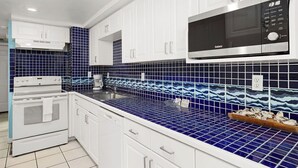 Een keuken met witte kastjes, een magnetron en een blauwe betegelde achterwand.