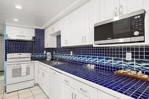 A kitchen with white cabinets, a microwave, and blue-tiled backsplash. - Aquarius by South Padre Resort Rentals (South Padre Island)