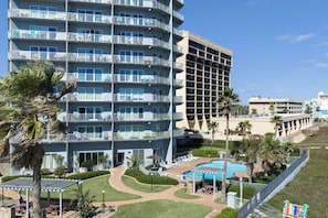 A multi-story hotel with balconies, a swimming pool, and palm trees. - Aquarius by South Padre Resort Rentals (South Padre Island)