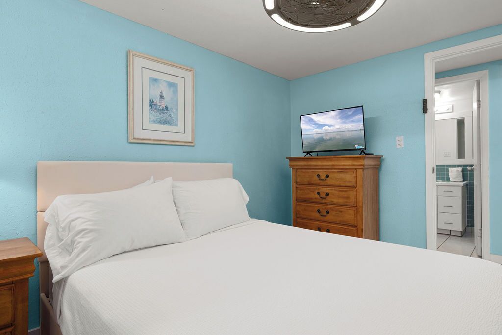 A bedroom with a bed, a dresser, a television, and a framed picture on the wall.