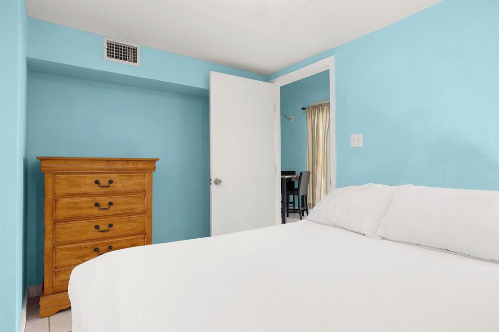 A bedroom with a bed, a wooden dresser, and a door leading to another room.