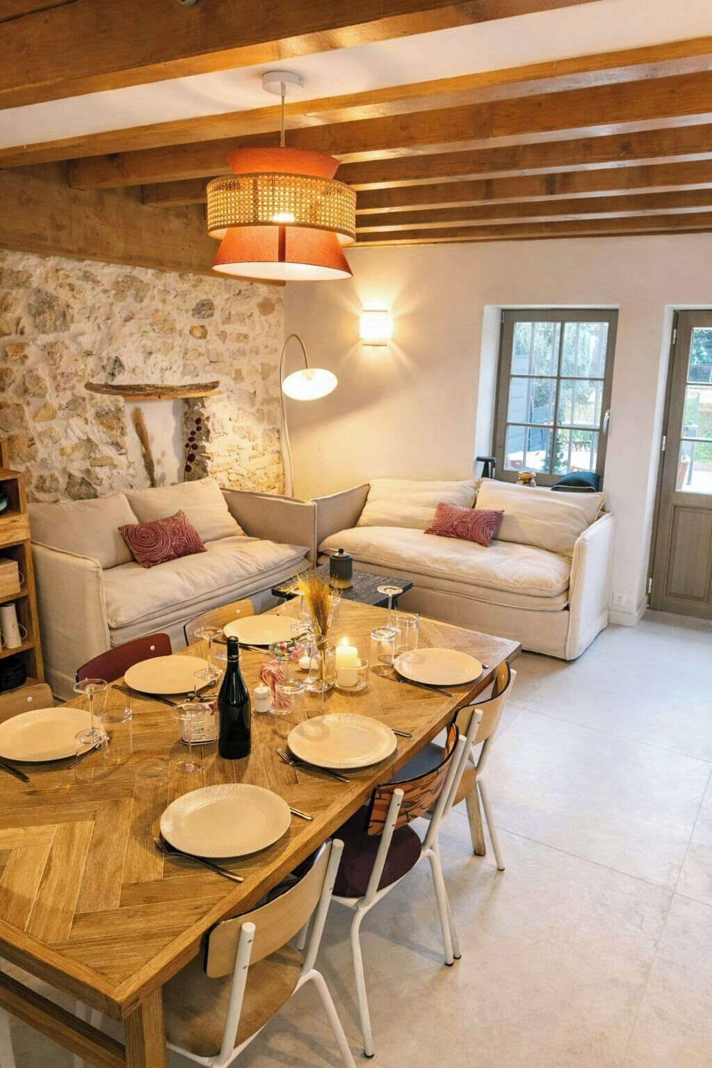 A dining area with a wooden table set for four, a stone wall, a wooden ceiling, and a sofa with cushions.