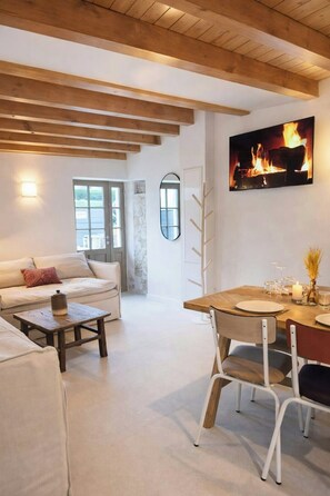 Ein modernes Wohnzimmer mit Holzboden, Kamin, einer Couch, einem Esstisch mit Stühlen und einem Spiegel an der Wand.