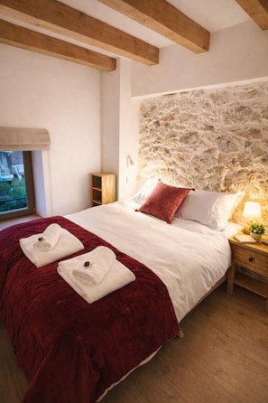 Ein Schlafzimmer mit Stewand, einem Holzbettgestell, einer roten Bettdecke, zwei Handtüchern, einem Nachttisch mit Lampe und einer kleinen Pflanze.