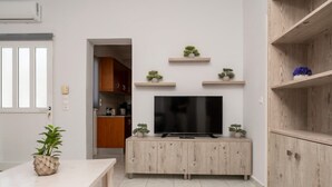Un salon moderne avec un téléviseur posé sur un meuble en bois, une table à manger agrémentée d’une plante, et une cuisine en arrière-plan.