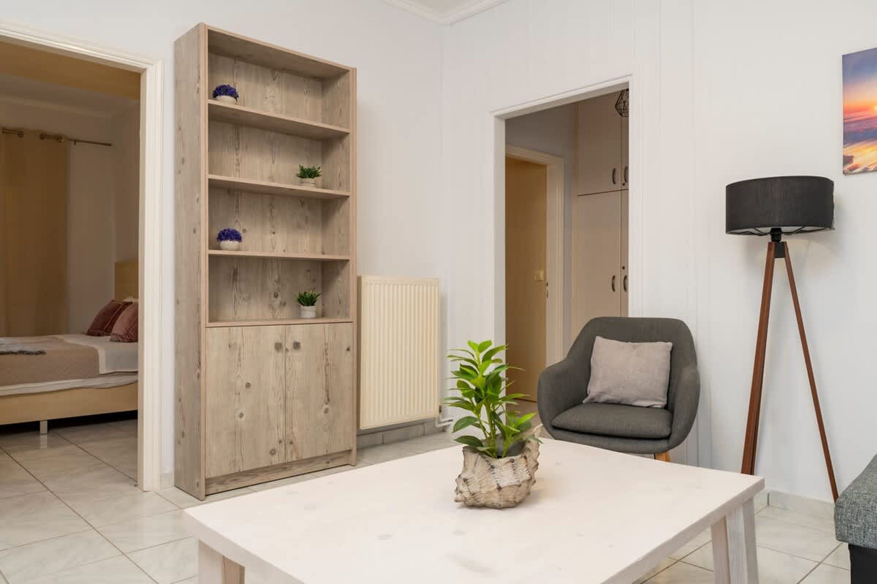Una stanza con un letto, una libreria in legno, una poltrona grigia, una lampada da terra e un tavolino con una pianta.