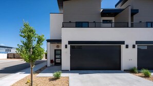 Ett modernt hus i två våningar med ett garage, ett litet träd och en klarblå himmel.