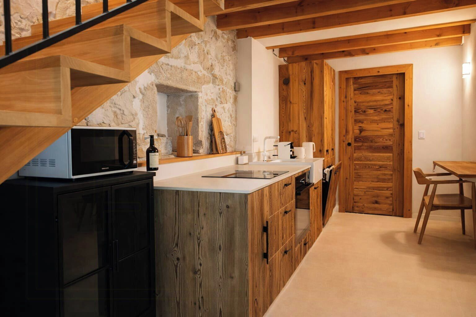 Eine Küche mit einer Steinwand, Holzschränken, einer Mikrowelle und einer Holztür.