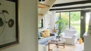 Una sala de estar moderna con un sofá, una mesa de centro y un sillón blanco. Se aprecia un ventanal con vistas a zonas verdes.