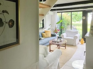 Ein modernes Wohnzimmer mit einer Couch, einem Couchtisch und einem weißen Sessel. Ein großes Fenster bietet Blick auf Grünflächen.