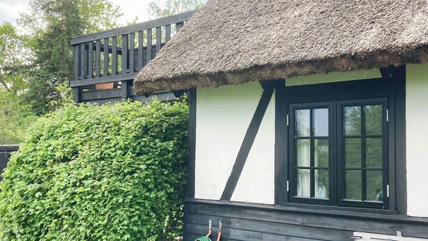 Una casa con techo de paja, ventana con marcos negros y una terraza de madera.