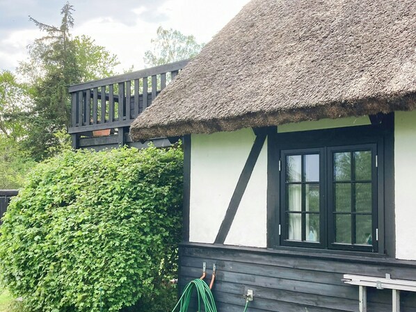 Ein Haus mit einem Strohdach, einem Fenster mit schwarzen Rahmen und einer Holzterrasse.