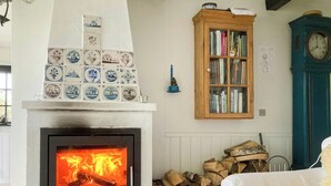 Una chimenea con fuego, una estantería, un reloj y una pila de leña.