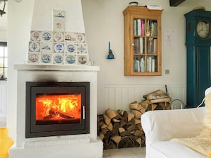 Ein Kamin mit Feuer, ein Bücherregal, eine Uhr und ein Holzstapel.