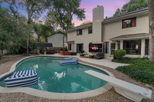 Ein Swimmingpool mit Liegestühlen, einer Sonnenterrasse und einem Haus, an dem das Netflix-Logo zu sehen ist.