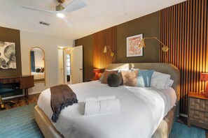 Ein helles Schlafzimmer mit einem großen Bett, Nachttischlampen, einem Schreibtisch und einem Spiegel.