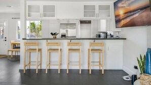 A modern kitchen with white cabinets, a central island with bar stools, stainless steel appliances, and a large window. - Harbor Isle Beauty - Minutes To Huntington Beach (Huntington Beach)