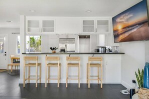A modern kitchen with white cabinets, a central island with bar stools, stainless steel appliances, and a large window. - Harbor Isle Beauty - Minutes To Huntington Beach (Huntington Beach)