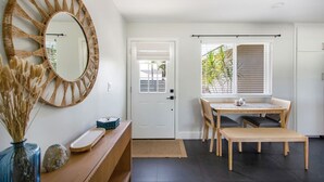 A modern interior with a round mirror, a dining table with chairs, a wooden console, and a view of greenery outside. - Harbor Isle Beauty - Minutes To Huntington Beach (Huntington Beach)