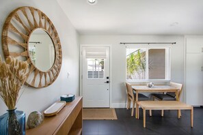 A modern interior with a round mirror, a dining table with chairs, a wooden console, and a view of greenery outside. - Harbor Isle Beauty - Minutes To Huntington Beach (Huntington Beach)