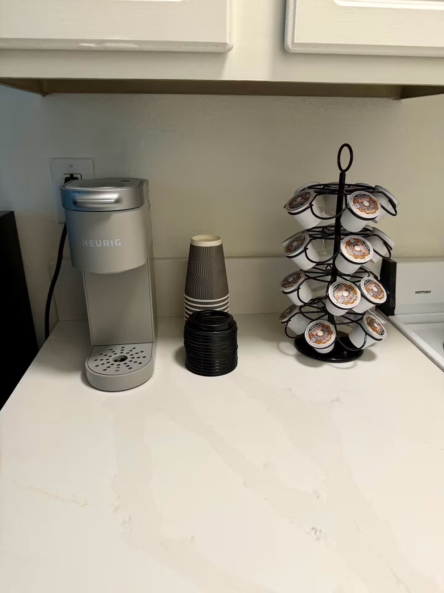 Uma bancada de cozinha com uma cafeteira Keurig, uma pilha de sousbicos pretos e um suporte de canecas com várias xícaras.