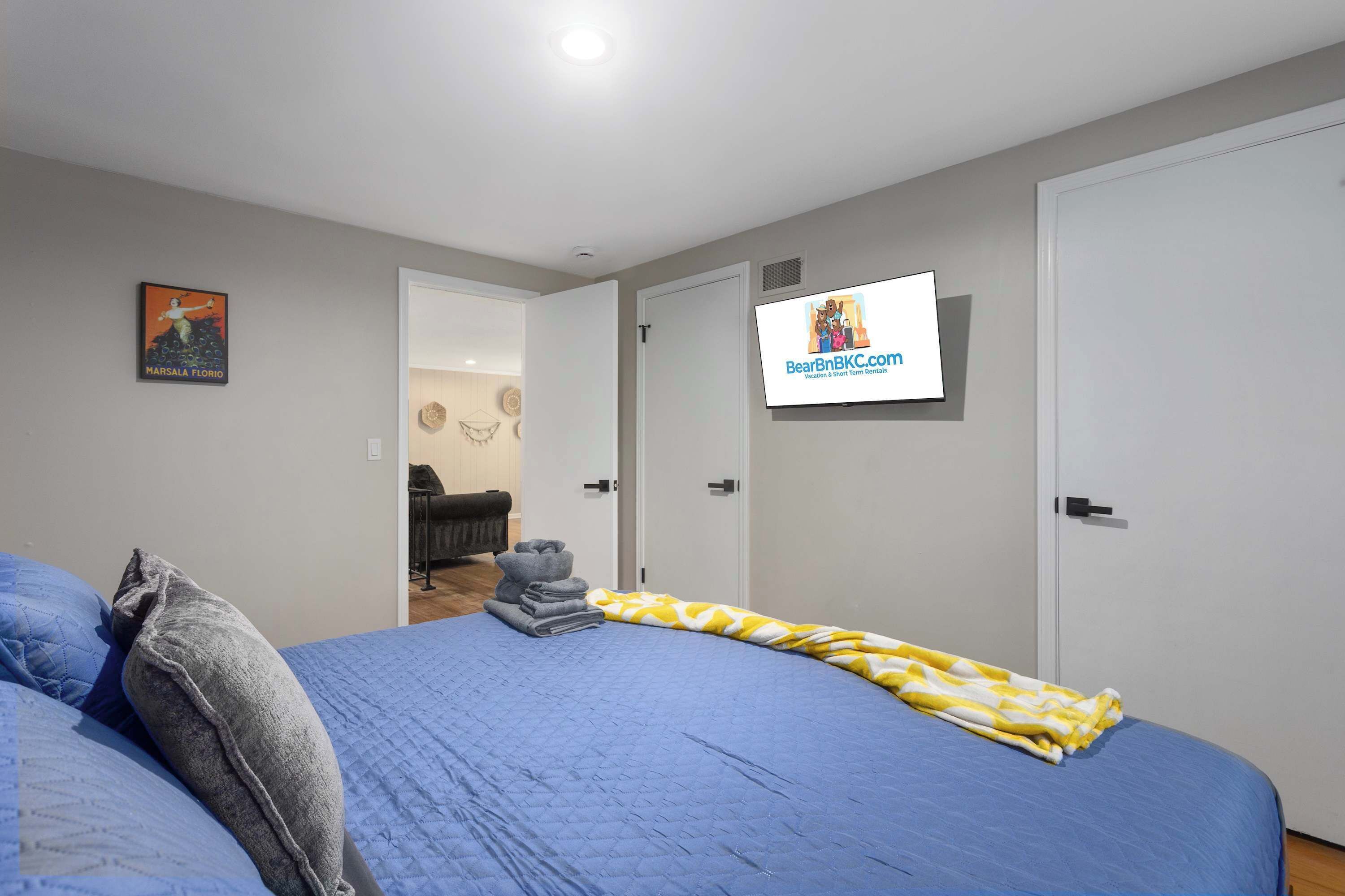 A bedroom with a bed, a TV mounted on the wall, and a door leading to another room.