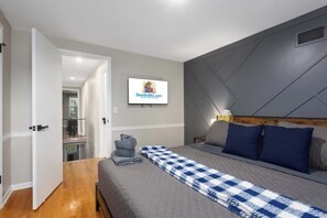 Ein Schlafzimmer mit einem Bett, einem Fernseher, einer karierten Decke und einem grauen Kopfteil.