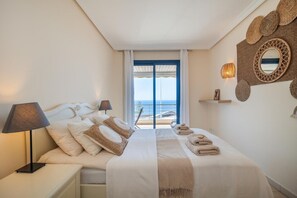 Ein Schlafzimmer mit Bett, Nachttischlampen, Blick aufs Meer und Wanddekoration.
