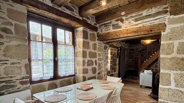 A rustic dining area with a long table, wicker chairs, and stone walls.
