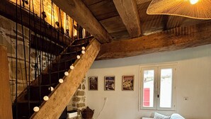 A rustic interior with a wooden staircase, a white sofa, a small round table, and framed pictures on the wall.