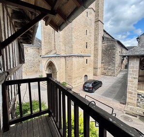 A stone building with a tower, a car parked in front, and a wooden balcony.