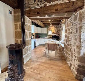 Une cuisine rustique aux murs de pierre, avec des poutres en bois et un coin repas comprenant une table et des chaises.