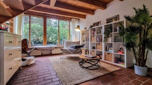 Ein gemütliches Zimmer mit großem Fenster, Bücherregal, Sessel und kleinem Tisch.