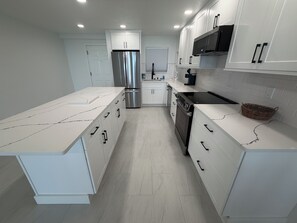 A modern kitchen with white cabinetry, stainless steel appliances, and a marble countertop. - Shores Club 1004 (Daytona Beach Shores)