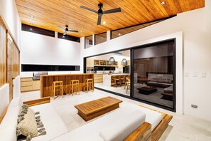 Ein modernes Interieur mit Holzbalkendecke, einer Küche mit Barhocker, einem Sofa und einer großen Schiebeglasdoor, die in einen Wohnbereich f ührt.