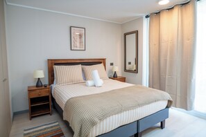 A neatly arranged bedroom with a bed, bedside tables, a mirror, and a window with curtains. - Downtown Suites by Andes+ (Santiago)