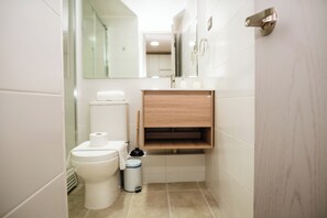 A modern bathroom with a toilet, sink, mirror, and storage cabinet. - Downtown Suites by Andes+ (Santiago)