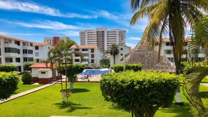 A hotel courtyard with a swimming pool, palm trees, and a view of high-rise buildings. - La Marina Condominios by Monyxbnb (Puerto Vallarta)