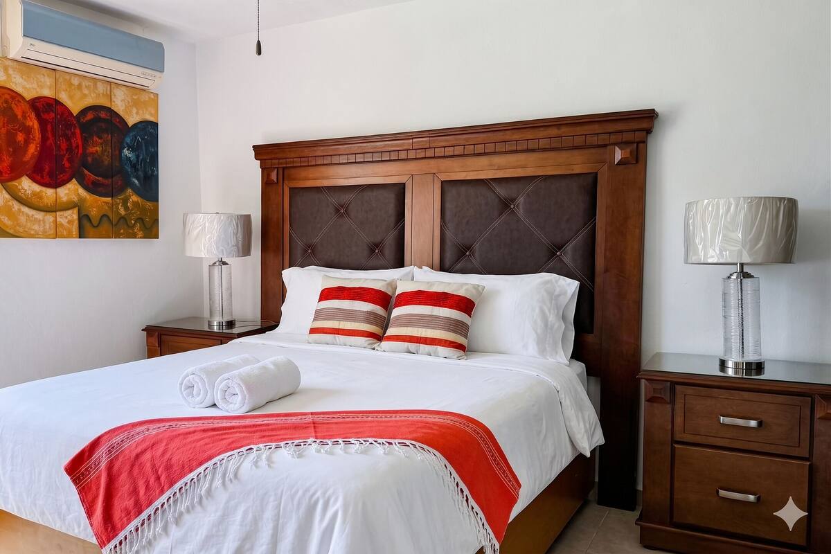 A neatly made bed with white linens, a red and white striped throw blanket, and two pillows with red and beige stripes.