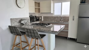 A kitchen with a granite countertop, stainless steel appliances, and wooden chairs. - La Marina Condominios by Monyxbnb (Puerto Vallarta)