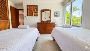 A hotel room with two beds, a wooden dresser, a mirror, and a window with a view of palm trees. - La Marina Condominios by Monyxbnb (Puerto Vallarta)