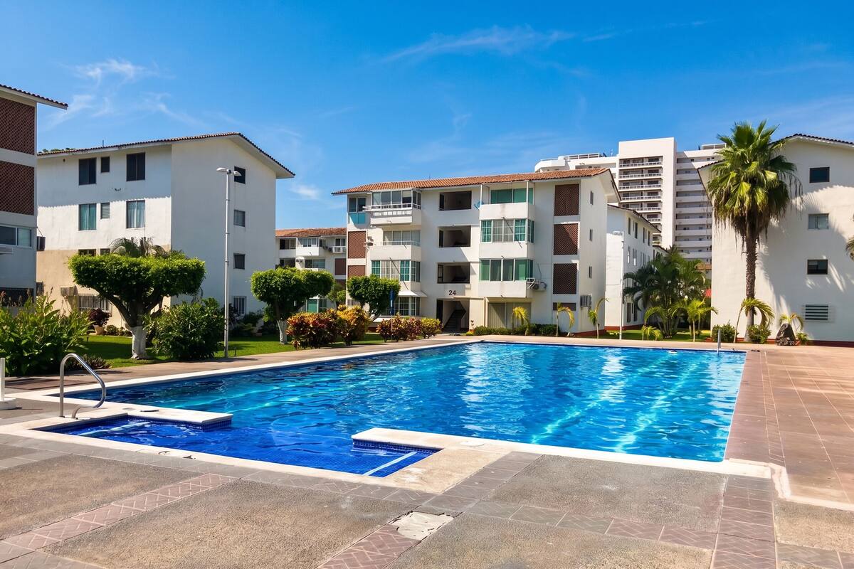 A swimming pool with a clear blue water, surrounded by a tiled deck.